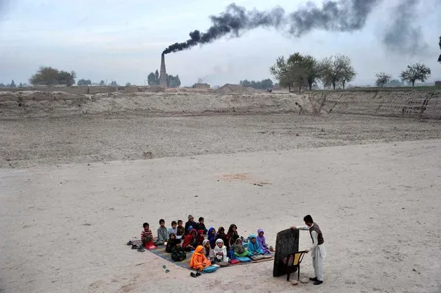 Afghan schoolchildren take lessons in an open classroom at a refugee camp on the outskirts of Jalalabad, Nangarhar province on December 1, 2013. Afghanistan has had only rare moments of peace over the past 30 years, its education system being undermined by the Soviet invasion of 1979, a civil war in the 1990s and five years of Taliban rule. (Photo by Noorullah Shirzada/AFP Photo)