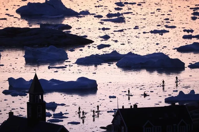 People ride stand-up paddle boards past floating ice and icebergs in Disko Bay on September 02, 2021 in Ilulissat, Greenland. Greenland in 2021 is experiencing one of its biggest ice-melt years in recorded history. Scientists studying the Greenland Ice Sheet observed rainfall on the highest point in Greenland for the first time ever in August. Researchers from Denmark estimated that in July of this year, enough ice melted on the Greenland Ice Sheet to cover the entire state of Florida with two inches of water. The observations come on the heels of the recent United Nations report on global warming which stated that accelerating climate change is driving an increase in extreme weather events. (Photo by Mario Tama/Getty Images)