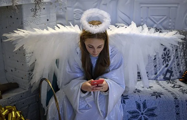A woman dressed as an angel takes a break from greeting children at a public library in Irpin, northwest of Kyiv, on December 23, 2022, amid the Russian invasion of Ukraine. (Photo by Genya Savilov/AFP Photo)