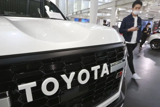 A man walks by the logo on a Toyota car at a showroom in Tokyo on October 18, 2021. Toyota says it is testing hydrogen combustion engines in race cars as it works toward commercial applications of the technology. Such engines burn hydrogen as fuel instead of gasoline, much like rockets. (Photo by Koji Sasahara/AP Photo)