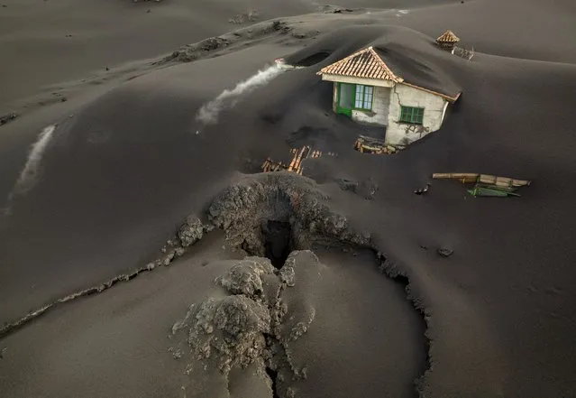 A fissure is seen next to a house covered with ash on the Canary island of La Palma, Spain, Wednesday, December 1 2021. A fissure that volcanologists believe spouted a gusher of lava left a gaping hole in front of house whose bottom floor was completely covered by a mountain of ash. A fresh stream of lava from volcano on Spain's La Palma threatened on Wednesday to engulf a parish church that has so far survived the eruption that shows no signs of relenting in its tenth week. (Photo by Emilio Morenatti/AP Photo)