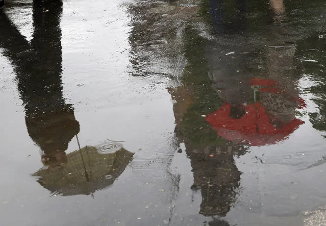 People are reflected in a puddle as they walk carrying umbrellas in Milan, Italy, Monday, April 27, 2015. (Photo by Antonio Calanni/AP Photo)