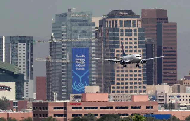 In this Monday, July 23, 2018 photo, heat ripples blur the downtown skyline as a jet lands in Phoenix, Ariz., as temperatures exceed 100 degrees in the morning hours. Already devilishly hot for being in the Sonoran desert, Arizona’s largest city is also an “urban heat island”, a phenomenon that pushes up temperatures in areas covered in heat-retaining asphalt and concrete. Phoenix officials say they are tackling urban warming, monitoring downtown temperatures, planting thousands of trees and capturing rainwater to cool off public spaces. (Photo by Matt York/AP Photo)