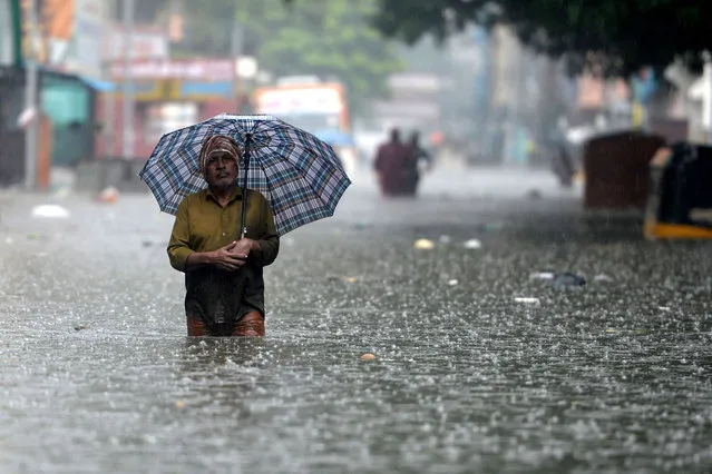 A man holds an umbrella as he wades through a flooded street after heavy monsoon rains in Chennai on November 8, 2021. (Photo by Arun Sankar/AFP Photo)