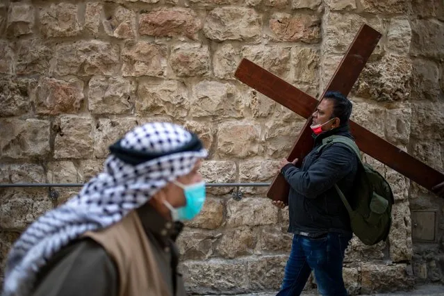 A Christian carries a cross as he walks along the Via Dolorosa towards the Church of the Holy Sepulchre, traditionally believed by many to be the site of the crucifixion of Jesus Christ, during the Good Friday procession in Jerusalem's old city, Friday, April 2, 2021. (Photo by Ariel Schalit/AP Photo)