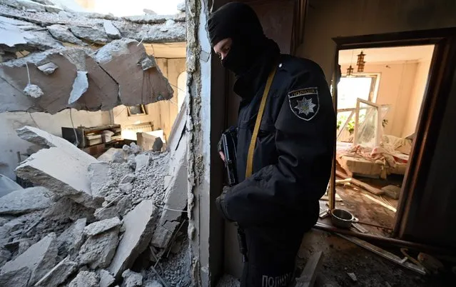 A police officer stands inside a destroyed apartment at a damaged housing block after it was hit by debris from a downed rocket in Kyiv on March 17, 2022, as Russian forces press in on the Ukrainian capital. Russian troops trying to encircle Kyiv have launched early morning strikes on the city for several successive days, putting traumatised residents further on edge. (Photo by Genya Savilov/AFP Photo)