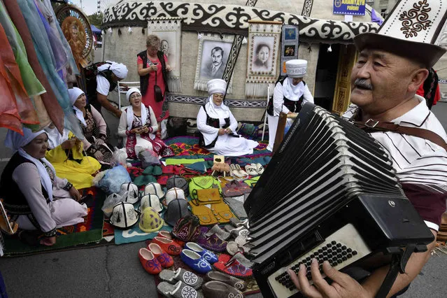 A Kyrgyz man plays accordion as women wearing traditional Kyrgyz clothes and headdresses called “elechek” sing a song as they celebrate Independence Day on Ala-Too Square in the center of Bishkek, Kyrgyzstan, Tuesday, August 31, 2021. The Central Asian nation of Kyrgyzstan marks the 30th anniversary of independence from the Soviet Union with a parade in central Bishkek. (Photo by Vladimir Voronin/AP Photo)