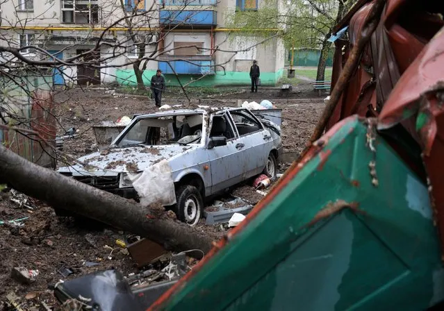 Local residents look at a destroyed car next to a multi-storey building in Lysychansk in the Luhansk region on April 13, 2022. (Photo by Anatolii Stepanov/AFP Photo)