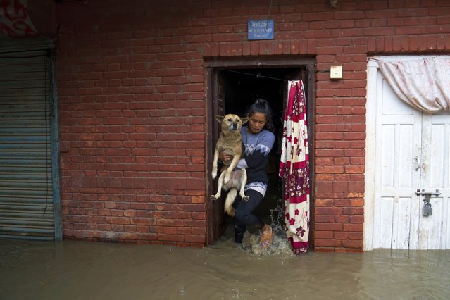 A woman carries her dog out from her flooded home following heavy monsoon rains in Kathmandu, Nepal, July 6, 2024. (Photo by Niranjan Shrestha/AP Photo)