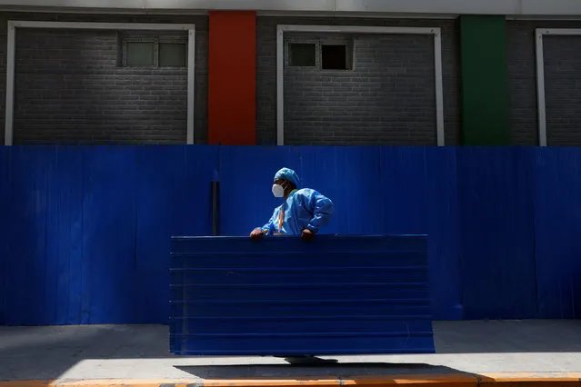 A worker wearing personal protective equipment (PPE), carries a metal sheet while installing a barricade around a residential area under lockdown, amid the coronavirus disease (COVID-19) outbreak in Beijing, China, May 4, 2022. (Photo by Carlos Garcia Rawlins/Reuters)