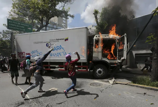 Masked demonstrators throw bottles at a government vehicle they seized, defaced and then set on fire after a cordon of police keep them from marching to the office of Attorney General Luisa Ortega Diaz to show their support for the one-time government loyalist, in Caracas, Venezuela, Thursday, June 22, 2017. Venezuela's Supreme Court cleared the way for the prosecution of the country's chief prosecutor, who became a surprise hero to the opposition after breaking ranks with the government of President Nicolas Maduro over his efforts to concentrate power. (Photo by Fernando Llano/AP Photo)