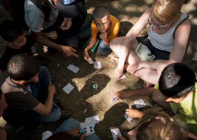 Volunteers play cards with migrant children in front of the Berlin State Office for Health and Social Affairs while waiting with other newly arrived refugees to apply for asylum in Berlin, August 10, 2015. (Photo by Stefanie Loos/Reuters)