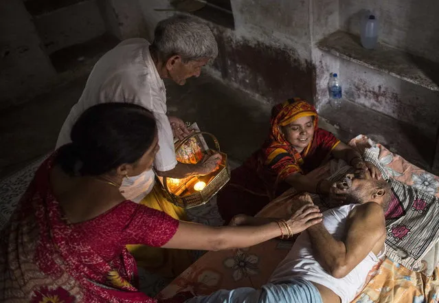 Kishore Pandey, 82, lies on a bed as his daughter, Usha Tiwari, holds him and a priest stands by them (L) at Mukti Bhavan (Salvation House) in Varanasi, in the northern Indian state of Uttar Pradesh, June 19, 2014. (Photo by Danish Siddiqui/Reuters)