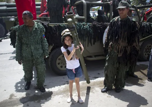 A girl poses for photos with soldiers and a weapon at the end of a military parade marking Venezuela's Independence Day in Caracas, Venezuela, Tuesday, July 5, 2016. Venezuela is marking 205 years of independence. (Photo by Ariana Cubillos/AP Photo)