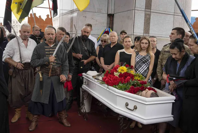 Relatives and friends attend the funeral of officers Andriy Zhovanyk and Yuri Kovalenko, who were killed in a battle against the Russian troops, in central Independence square in Kyiv, Ukraine, Friday, August 5, 2022. The honour guard dressed as Ukrainian Cossacks stand at left. (Photo by Efrem Lukatsky/AP Photo)
