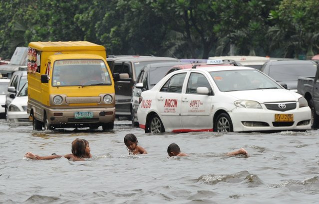 Children play in a flooded street caused by heavy rains overnight while motorists drive past in Manila on August 26, 2014. The weather bureau issued a yellow rain warning in the metropolis early on August 26, due to a low pressure area in the region of Bicol, southeast of Manila. (Photo by Ted Aljibe/AFP Photo)