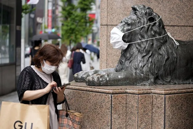 A shopper wearing a face mask checks her mobile phone beside a masked lion statue of a department store in Ginza shopping district in Tokyo Tuesday, August 30, 2022. (Photo by Shuji Kajiyama/AP Photo)