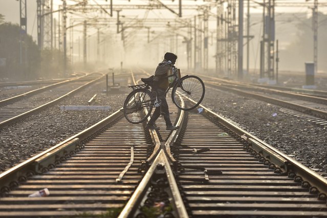 A man carries his bicycle as he crosses a railway track in a wintry morning near a train station in Jalandhar on December 26, 2024. (Photo by Shammi Mehra/AFP Photo)
