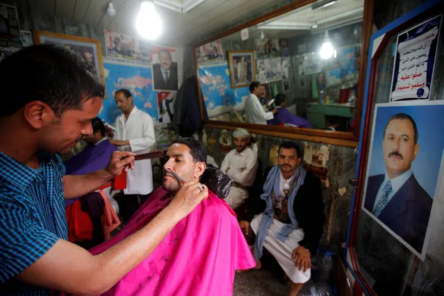 A barber works in his barbershop with a poster of Yemen's former President Ali Abdullah Saleh seen on its wall at the old quarter of the city of Sanaa, Yemen, July 24, 2016. (Photo by Mohamed al-Sayaghi/Reuters)