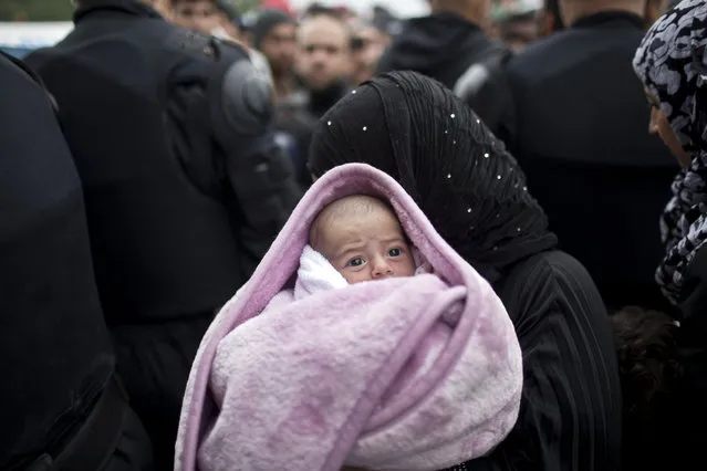 A woman carries a baby as she goes through a police line in front of a reception center in Opatovac, Croatia, Tuesday, September 22, 2015. Scuffles have broken out between Croatian police and asylum-seekers after they were barred from entering a newly opened reception center meant to register those seeking sanctuary in Europe. (Photo by Marko Drobnjakovic/AP Photo)