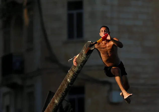 A man tries to grab a flag on the “gostra”, a pole covered in grease, during the religious feast of St Julian, patron of the town of St Julian's, outside Valletta, Malta, August 28, 2016. In the traditional “gostra”, a game stretching back to the Middle Ages, young men, women and children have to make their way to the top and try to uproot one of the flags to win prizes. From May to September in Malta, there is hardly any weekend when a town or a village is not celebrating the feast of its patron saint or other saints revered in different churches. (Photo by Darrin Zammit Lupi/Reuters)