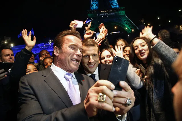 France's President Emmanuel Macron, center, and Arnold Schwarzenegger take a selfie with young people in front of the Eiffel Tower illuminated in green, aboard a boat cruising on the Seine river back from the One Planet Summit, Paris, Tuesday, December 12, 2017. More than 50 world leaders are gathering in Paris for a summit that President Emmanuel Macron hopes gives new momentum to the fight against global warming despite U.S. President Donald Trump's rejection of the Paris climate accord. (Photo by Thibault Camus/AP Photo)