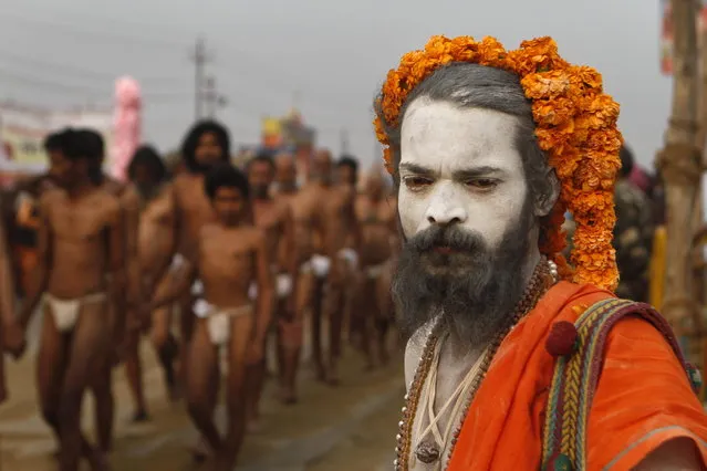 A Naga Sadhu, right, watches as Hindu holy men of the Juna Akhara sect arrive for a rituals that are believed to rid them of all ties in this life and dedicate themselves to serving God as a 'Naga' or naked holy men, at Sangam, the confluence of the Ganges and Yamuna River during the Maha Kumbh festival in Allahabad, India, Wednesday, February6, 2013. The significance of nakedness is that they will not have any worldly ties to material belongings, even something as simple as clothes. This ritual that transforms selected holy men to Naga can only be done at the Kumbh festival. (Photo by Rajesh Kumar Singh/AP Photo)