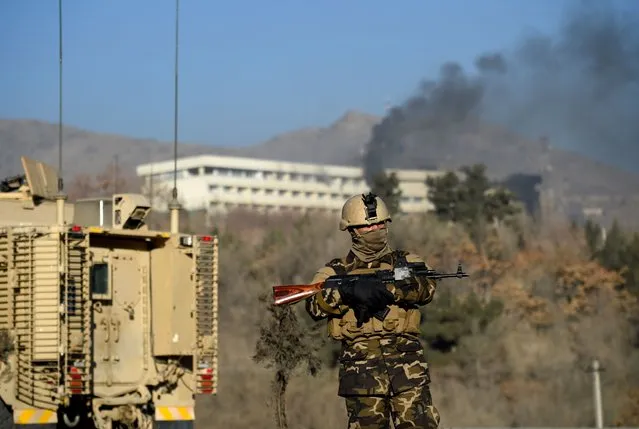 An Afghan security personnel stands guard as smoke billows from the Intercontinental Hotel during a fight between gunmen and Afghan security forces in Kabul on January 21, 2018. Gunmen stormed a luxury hotel in Kabul killing at least six people, including a foreigner, sparking a twelve hour fight with security forces that left terrified guests scrambling to escape and parts of the building ablaze. Afghan security forces killed four attackers during the night-time siege, interior ministry spokesman Najib Danish told Tolo News, during which people trapped inside the landmark hotel were seen climbing over balconies to escape. (Photo by Wakil Kohsar/AFP Photo)