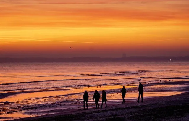 People walk on the beach along the Baltic Sea in Scharbeutz, northern Germany, before sunrise on Thursday, February 9, 2023. (Photo by Michael Probst/AP Photo)
