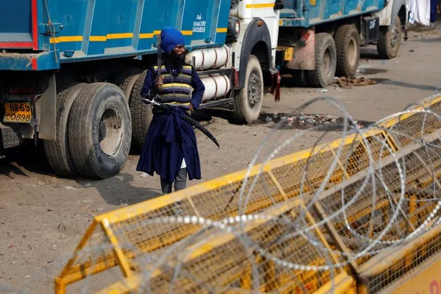 A Nihang (Sikh warrior) walks past police barricades at the site of a protest against the newly passed farm bills at Singhu border near New Delhi, India, December 7, 2020. (Photo by Adnan Abidi/Reuters)