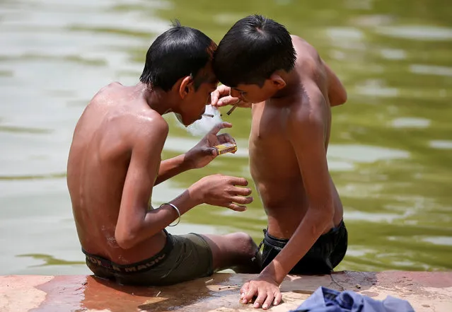 Boys smoke bidi, a local cigarette hand-rolled with tobacco leaf, after taking a dip in a pond to cool off on a hot summer day in New Delhi, India, May 31, 2018. (Photo by Amit Dave/Reuters)