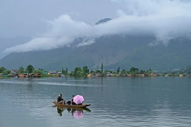 A woman steers a boat as she takes children to school during a rainy morning at the Dal lake in Srinagar on May 18, 2023. (Photo by Tauseef Mustafa/AFP Photo)