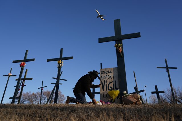 A plane takes off from Ronald Reagan Washington National Airport as Roberto Marquez of Dallas places flowers at a memorial of crosses he erected for the 67 victims of a midair collision between an Army helicopter and an American Airlines jet, Saturday, February 1, 2025, in Arlington, Va. (Photo by Carolyn Kaster/AP Photo)