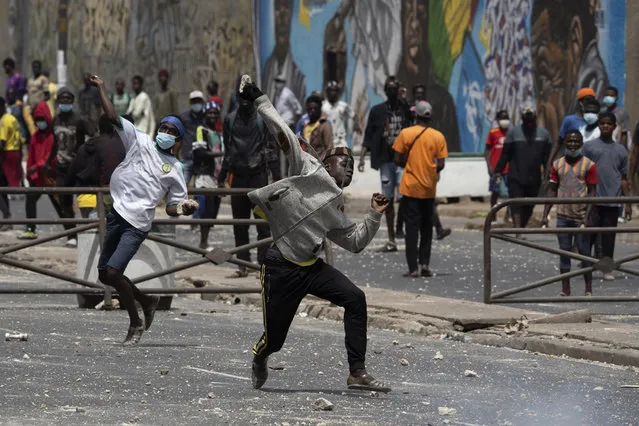 Demonstrators throw rocks at riot policemen during protests against the arrest of opposition leader and former presidential candidate Ousmane Sonko in Dakar, Senegal, Friday, March 5, 2021. (Photo by Leo Correa/AP Photo)