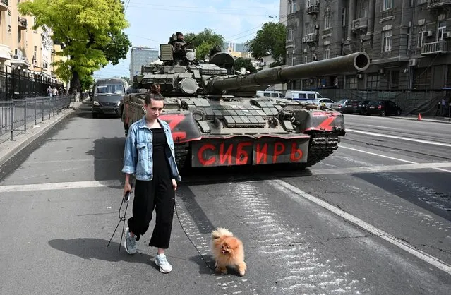 A woman with a dog walks past a tank as fighters of Wagner private mercenary group are deployed in a street near the headquarters of the Southern Military District in the city of Rostov-on-Don, Russia on June 24, 2023. A sign on a tank reads: “Siberia”. (Photo by Reuters/Stringer)