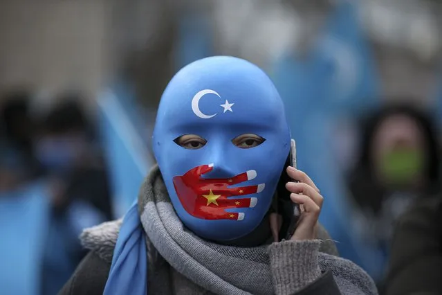 A protester from the Uyghur community living in Turkey, wearing a mask with a Chinese flag uses a mobile phone during a protest in Istanbul, Thursday, March 25, against against the visit of China's FM Wang Yi to Turkey. Hundreds of Uyghurs staged protests in Istanbul and the capital Ankara, denouncing Wang Yi's visit to Turkey and demanding that the Turkish government take a stronger stance against human rights abuses in China's far-western Xinjiang region. (Photo by Emrah Gurel/AP Photo)