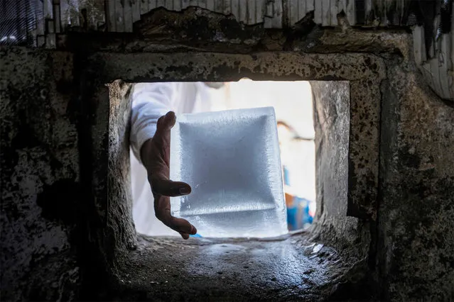 A man takes a block of ice out of an ice factory for sale in Iraq's southern city of Basra on July 8, 2023. (Photo by Hussein Faleh/AFP Photo)
