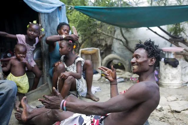 In this August 25, 2018 photo, Changlair Aristide jokes with a friend as his wife Violene Mareus does their 9-year-old daughter Changline's hair outside their home near the Truitier landfill where Aristide scavenges for valuable items to use or sell, in the Cite Soleil slum of Port-au-Prince, Haiti. Their other daughters Belinda, 3, and Viergeline, 5, stand in the doorway. (Photo by Dieu Nalio Chery/AP Photo)