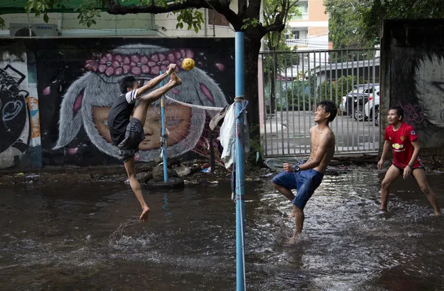 An airborne migrant worker kicks a rattan ball during a game of Chinlone in a field flooded by rain water in Bangkok, Thailand, Thursday, May 31, 2018. The popular Burmese sport Chinlone, a combination of sport and dance, is played between two teams consisting of six players each, passing a rattan ball back and forth with feet, knees and heads. (Photo by Gemunu Amarasinghe/AP Photo)