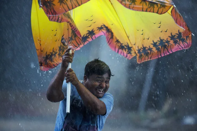 An Indian man reacts as he struggles to hold an umbrella against strong winds during a rain in Hyderabad, India, Wednesday, October 17, 2018. Monsoon season in India begins in June and ends in October. (Photo by Mahesh Kumar A./AP Photo)