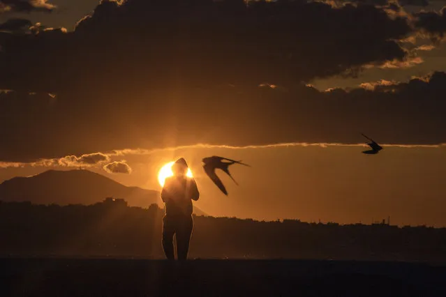 Birds fly as a man walks during a sunset in Alimos, a seaside suburb of Athens, on Tuesday, April 20, 2021. (Photo by Petros Giannakouris/AP Photo)