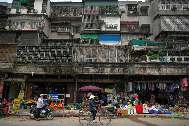 A woman rides her bicycle past shops beneath a residential building in Hanoi on March 31, 2021. (Photo by Manan Vatsyayana/AFP Photo)