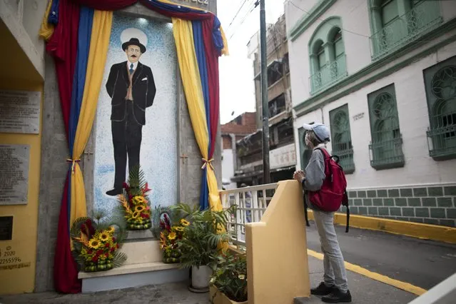 A woman prays close to a painting of Venezuelan popular saint, Dr. Jose Gregorio Hernandez at the street where he died in a car accident in 1919, in La Pastora neighborhood of Caracas, Venezuela, Wednesday, April 28, 2021. (Photo by Ariana Cubillos/AP Photo)