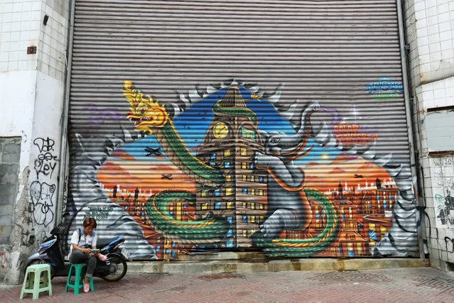A Thai woman reading on her mobile phone as she sits beside a graffiti on a gate of an abandoned mall in a popular tourist area in Bangkok, Thailand, 25 March 2015. The Thai economy was expected to grow more than three percent in the first quarter of 2015, boosted by a recovering tourism sector, increased private consumption and accelerated government spending. (Photo by Narong Sangnak/EPA)