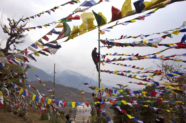 An exile Tibetan climbs a tall post to tie multicolor prayer flags called wind horse or “lungta” on the third day of the Tibetan New Year, in Dharmsala, India, Thursday, February 11, 2016. Tibetans believe that the Buddhist prayers printed on these flags whose colors represent the five elements, earth, fire, sky, water and air, are spread on wind. (Photo by Ashwini Bhatia/AP Photo)