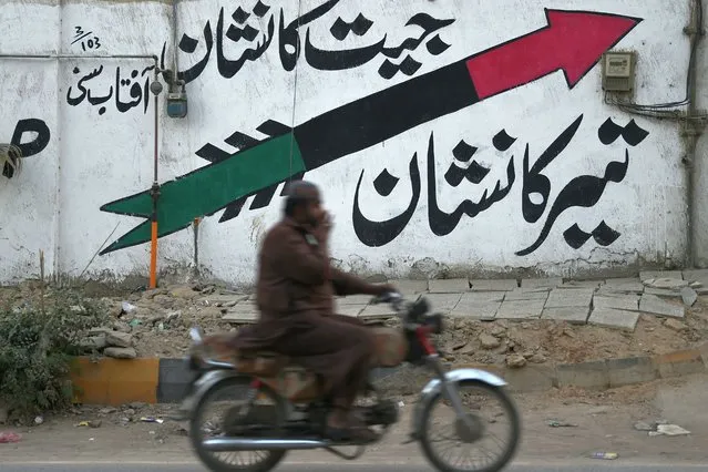 A motorcyclist rides past a wall painted with Pakistan People's Party (PPP) logo along a street in Karachi on January 12, 2024, ahead of the upcoming general elections. (Photo by Asif Hassan/AFP Photo)