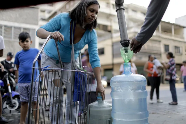 A woman fills a container with water from a truck in Caracas, Venezuela, Wednesday, March 27, 2019. After days of intermittent electricity supply in Venezuela, which affects the water supply, the people in the capital city have started to collect water from waterfalls and wells and carry it to their homes. (Photo by Natacha Pisarenko/AP Photo)