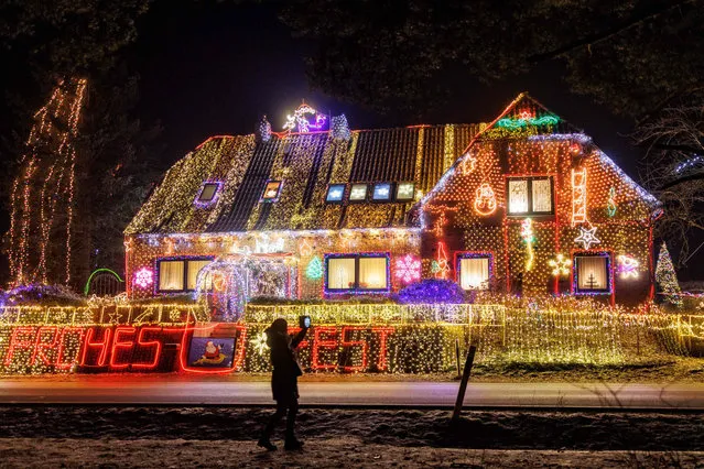 A woman takes a photo of a house illuminated with Christmas outdoor decoration in Buecken, northern Germany on December 16, 2022. (Photo by Axel Heimken/AFP Photo)