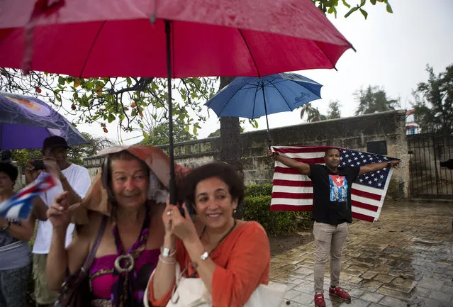A handful of Cubans gather along the Malecon sea wall under a steady rain to wave to U.S. President Barack Obama's convoy as it arrives in Old Havana, Cuba, Sunday, March 20, 2016. Obama's trip is a crowning moment in his and Cuban President Raul Castro's ambitious effort to restore normal relations between their countries. (Photo by Rebecca Blackwell/AP Photo)