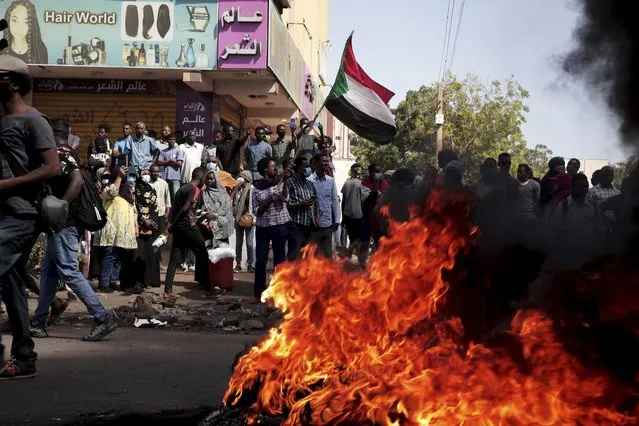 People chant slogans and burn tires during a protest to denounce the October 2021 military coup, in Khartoum, Sudan, Thursday, January 6, 2022. Sudanese took to the streets in the capital, Khartoum, and other cities on Thursday in anti-coup protests as the country plunged further into turmoil following the resignation of the prime minister earlier this week. (Photo by Marwan Ali/AP Photo)
